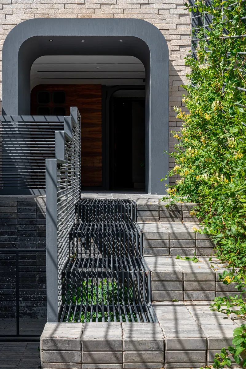 Entrance with rounded arch portal and metal walkway bridge casting dappled shadows in midday sun