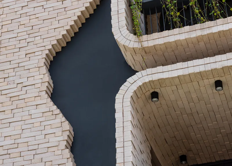 Upward view of curved brick soffits and recessed downlights meeting textured masonry wall
