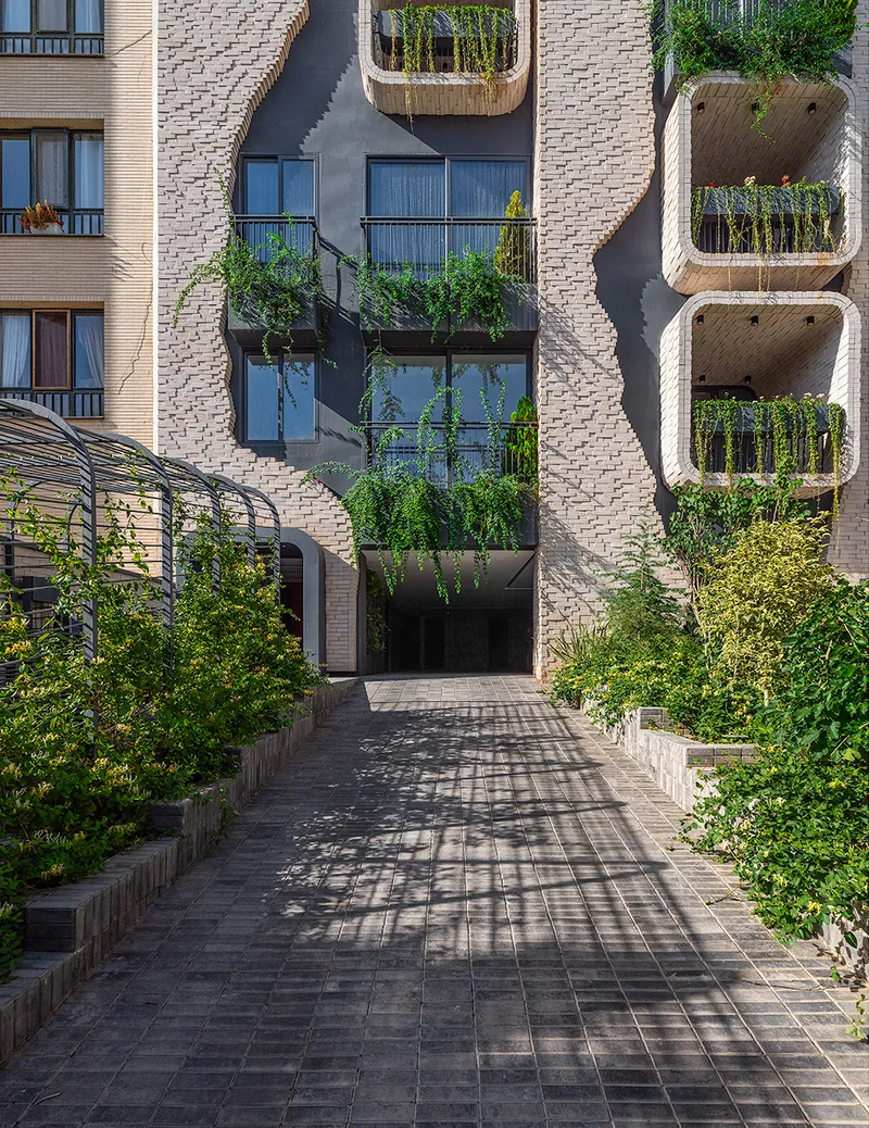 Paved courtyard pathway leading to facade with planted balconies and rounded window openings