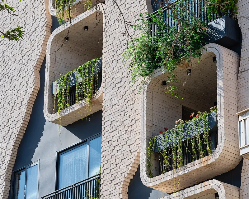 Stacked rounded-corner balconies with trailing plants set into a pale brick facade in bright sunlight