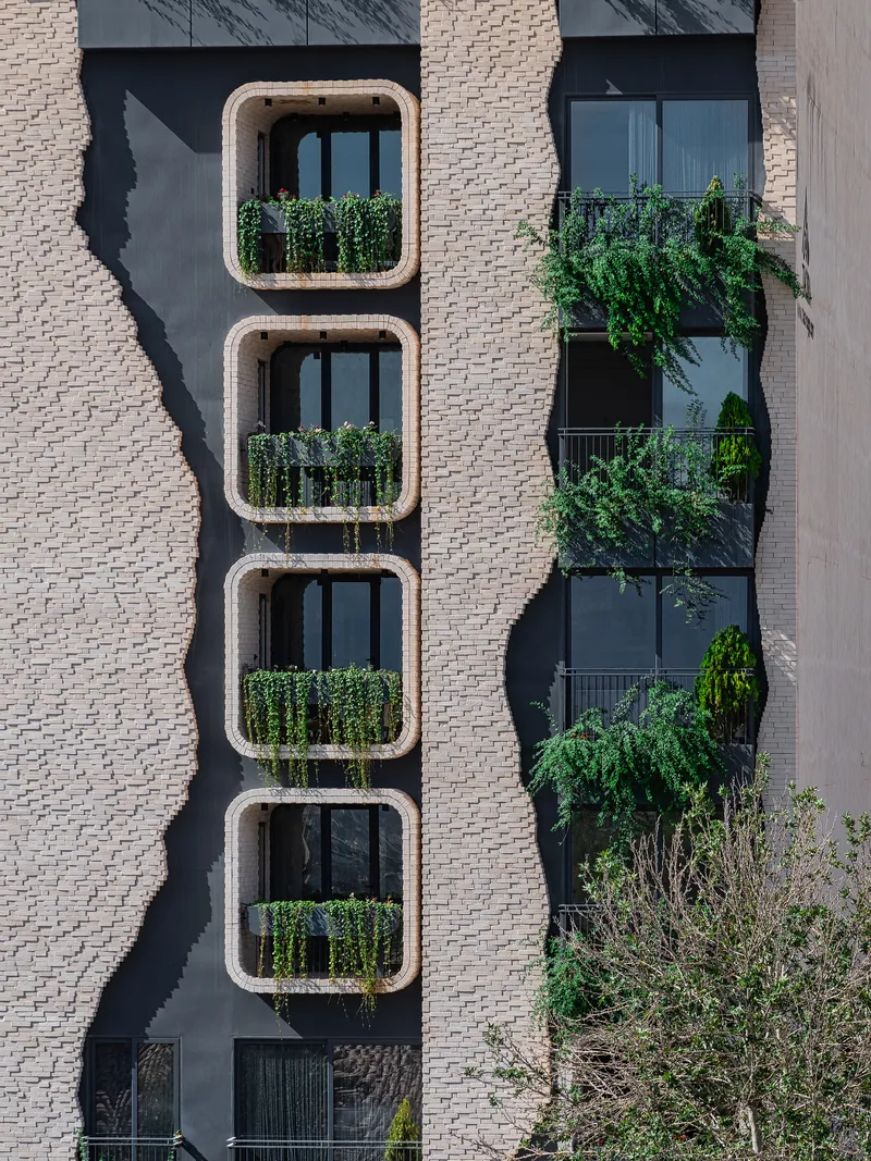 Vertical stack of four rounded-corner balconies with planted railings beside a cascading green facade