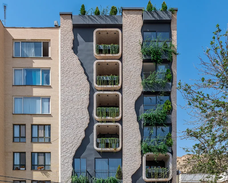 Street facade showing stacked rounded balconies with planted greenery between textured brick piers