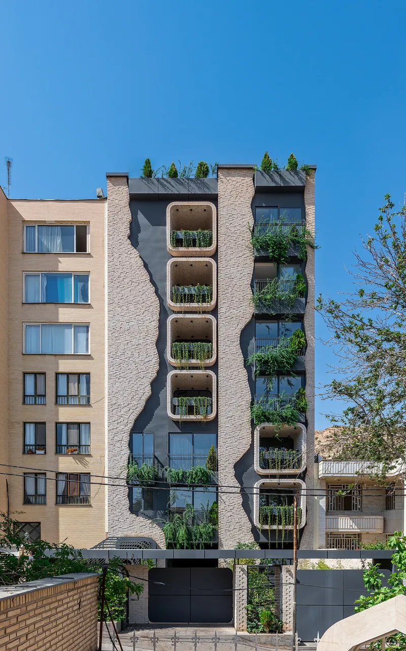 Full view of the residential facade with vertical stack of planted balconies under a clear sky