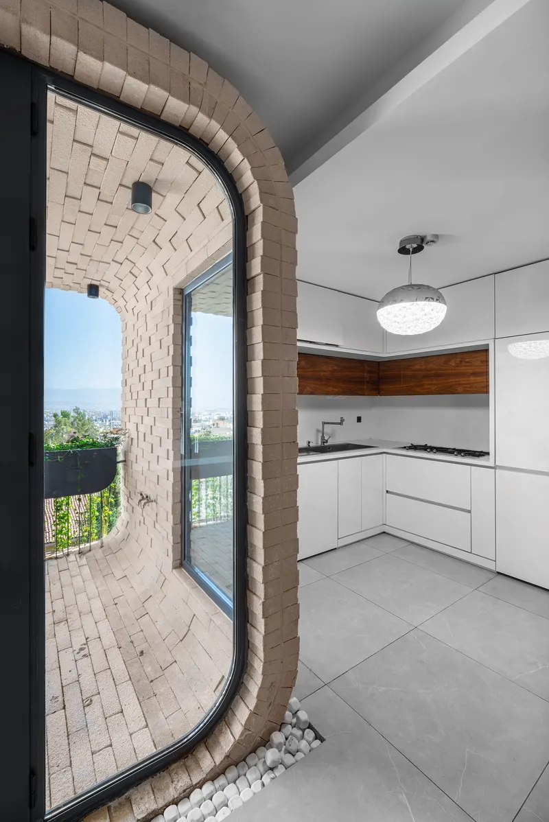 Curved brick archway opening from kitchen onto planted balcony with pebble drainage bed