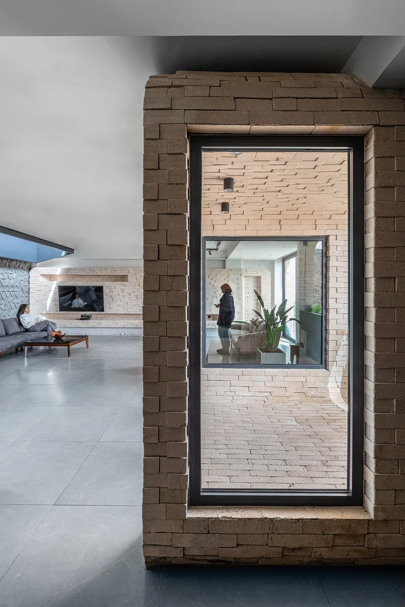 Interior view through brick-framed window opening showing a person standing in adjacent unit