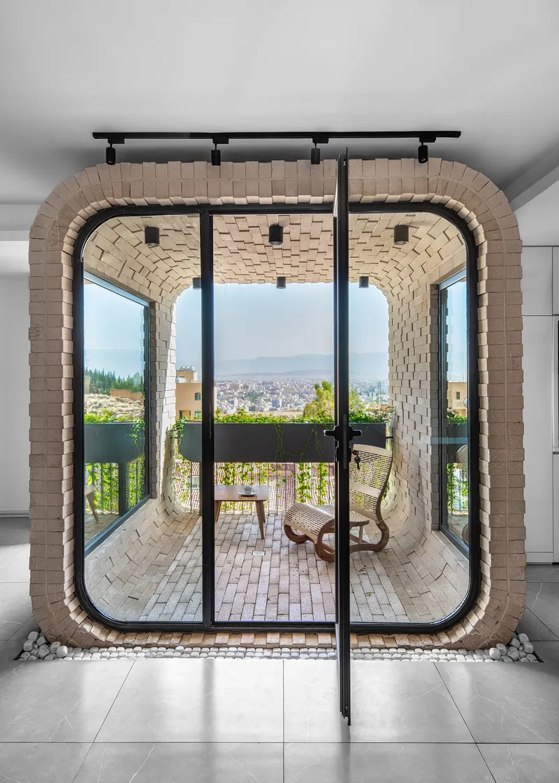 Interior view through glass doors to a vaulted brick balcony with seating and cityscape beyond