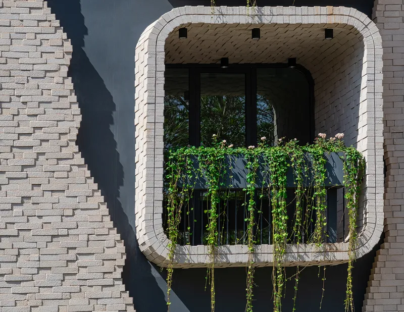 Close-up of a single balcony with vining plants on black railings framed by pale brick and recessed glazing