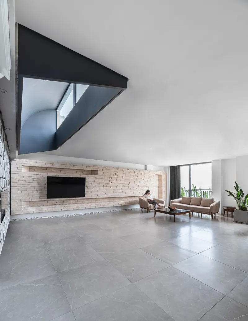 Double-height living room with textured brick wall and triangular black-framed mezzanine opening above