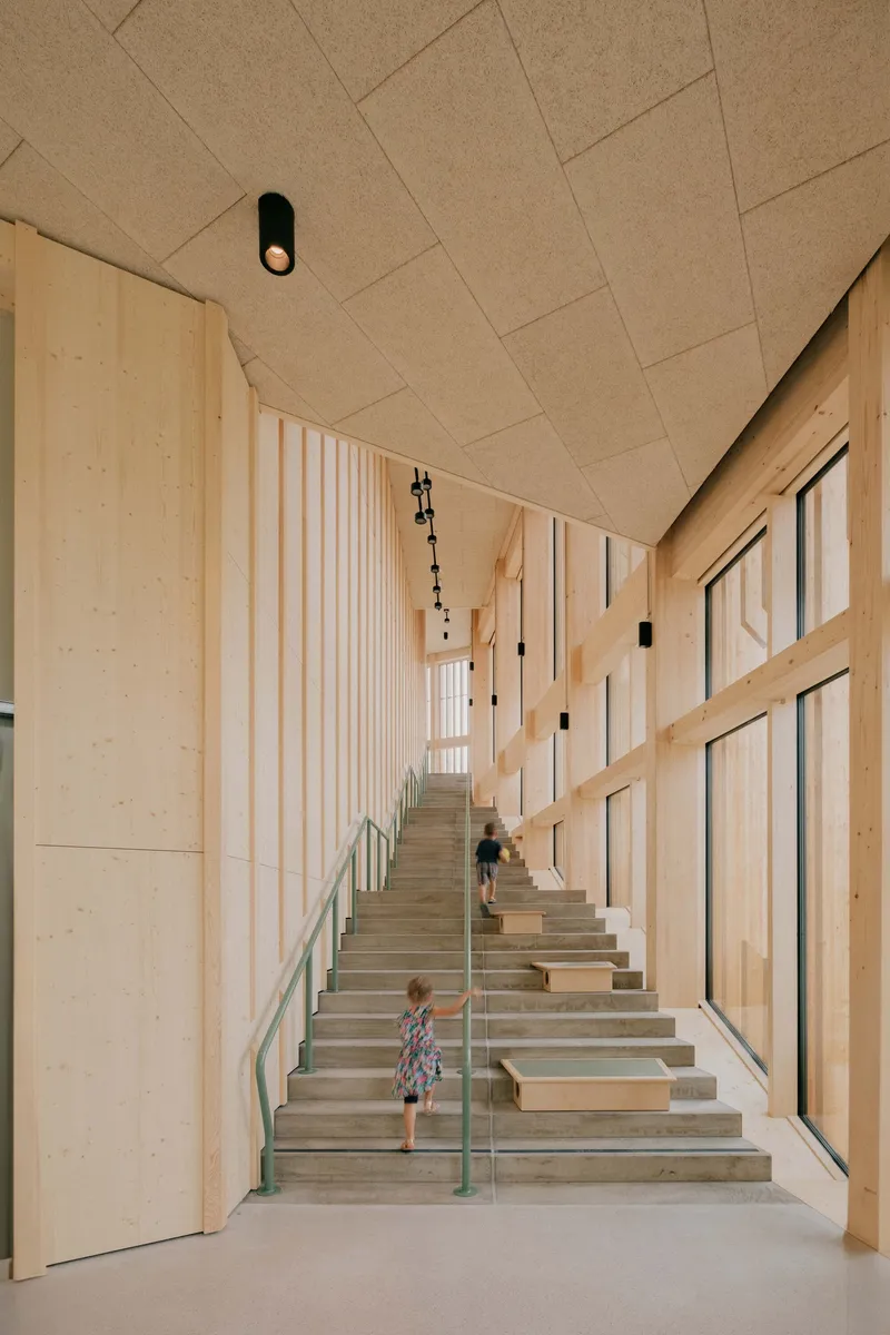 Timber-lined stairwell with diagonal acoustic ceiling panels and child descending the steps