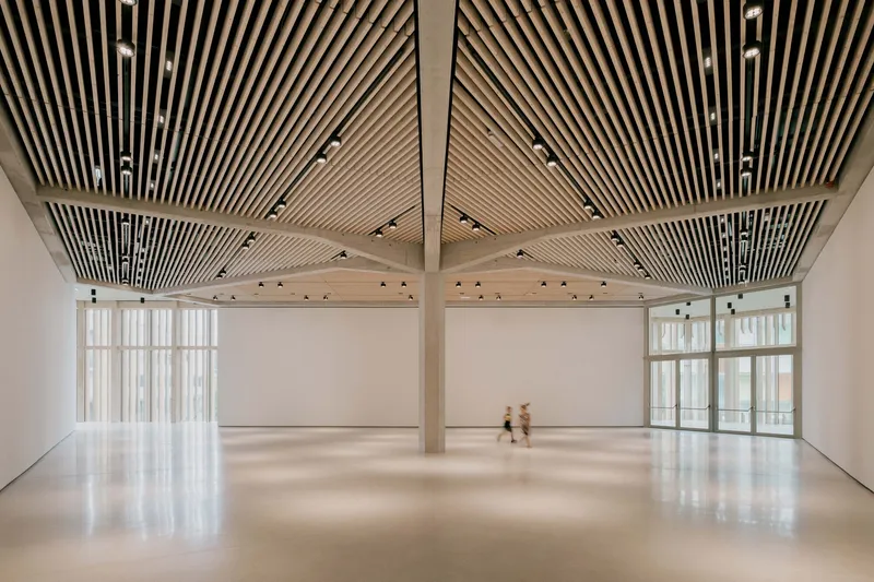 Open gallery space with radiating timber slat ceiling and two figures crossing the polished floor