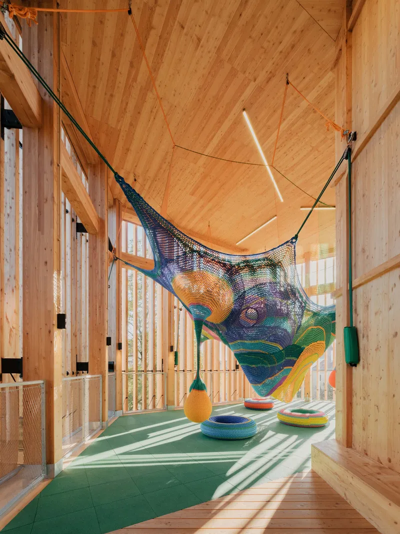 Play area with suspended mesh net installation over green floor mats beneath an exposed timber ceiling