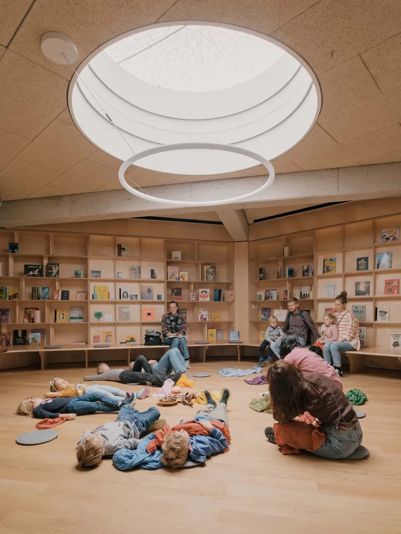 Library reading room with circular skylight and children sprawled on the wooden floor beneath book-filled shelves