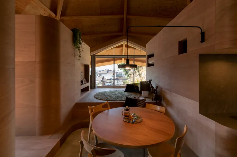 Dining area with round timber table beneath a gabled window framing a view of neighboring rooftops