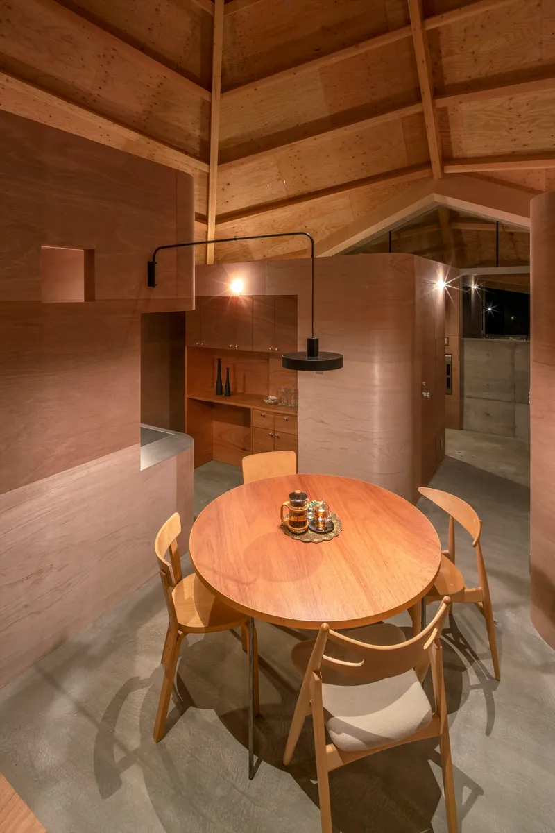 Round dining table on polished concrete floor beneath black pendant lamp and timber rafters at night
