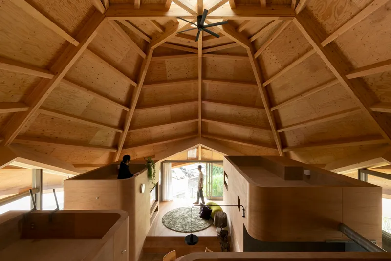 Upward view of the polygonal timber ceiling with exposed beams and central skylight above plywood room modules