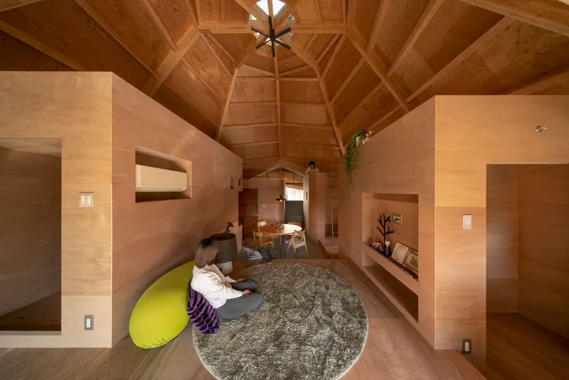 Interior showing plywood room volumes with recessed niches and a circular rug under the timber ceiling