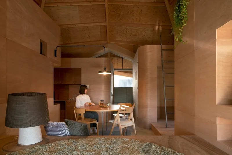 Dining area with timber table and chairs framed by plywood walls and pendant light fixture