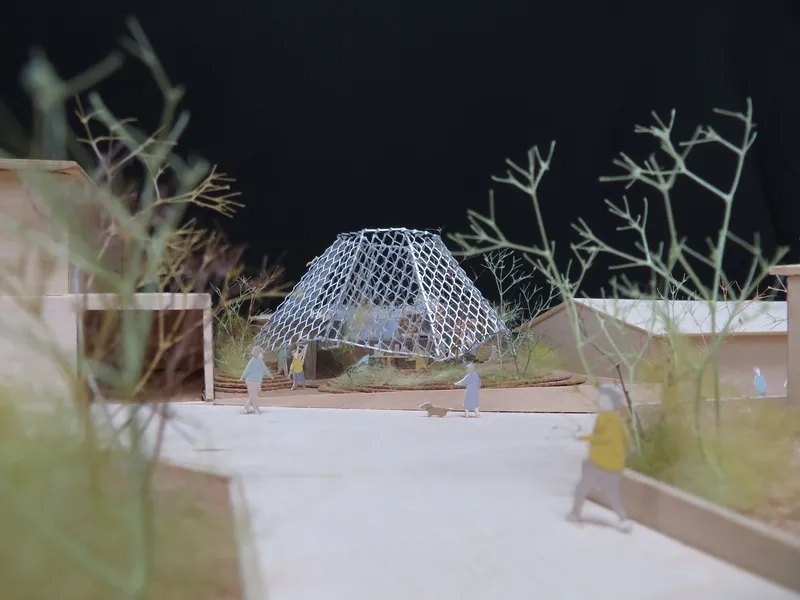 Physical model showing a geodesic dome pavilion with wire mesh structure surrounded by sparse vegetation and figures