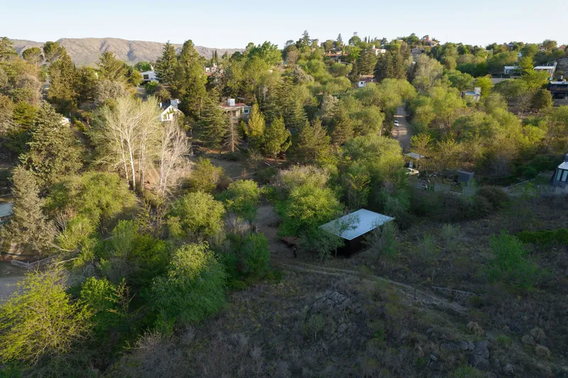 Aerial view of a low-profile structure amid dense vegetation on a hillside neighborhood