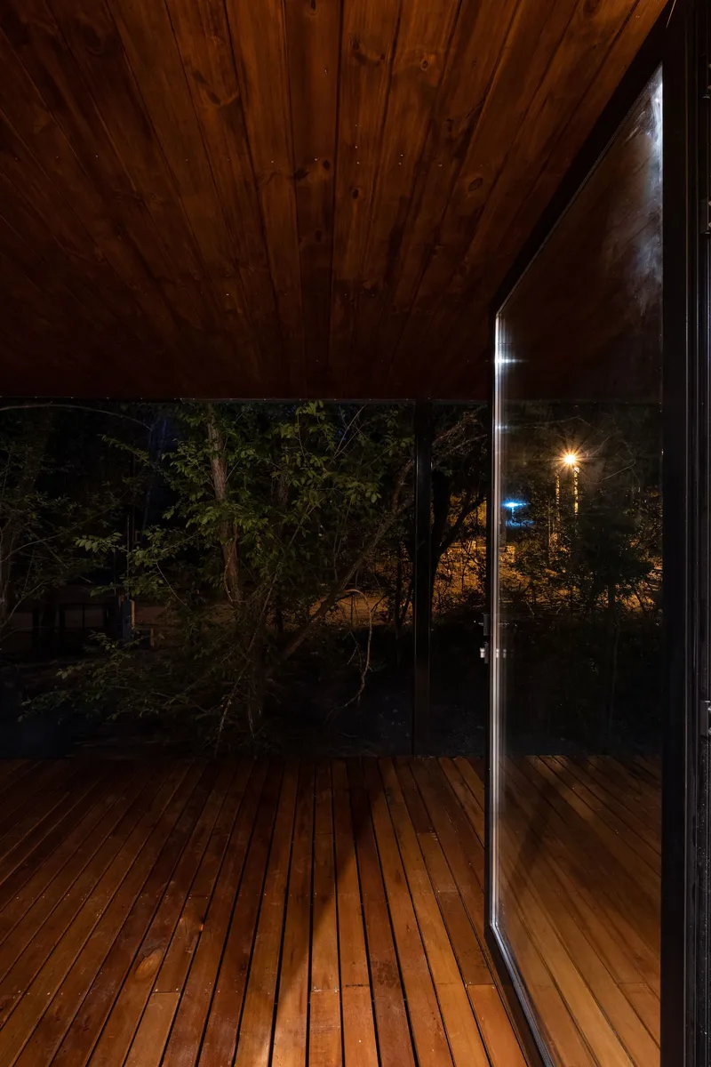 Wood-paneled ceiling over the terrace at dusk with glass doors reflecting the surrounding trees