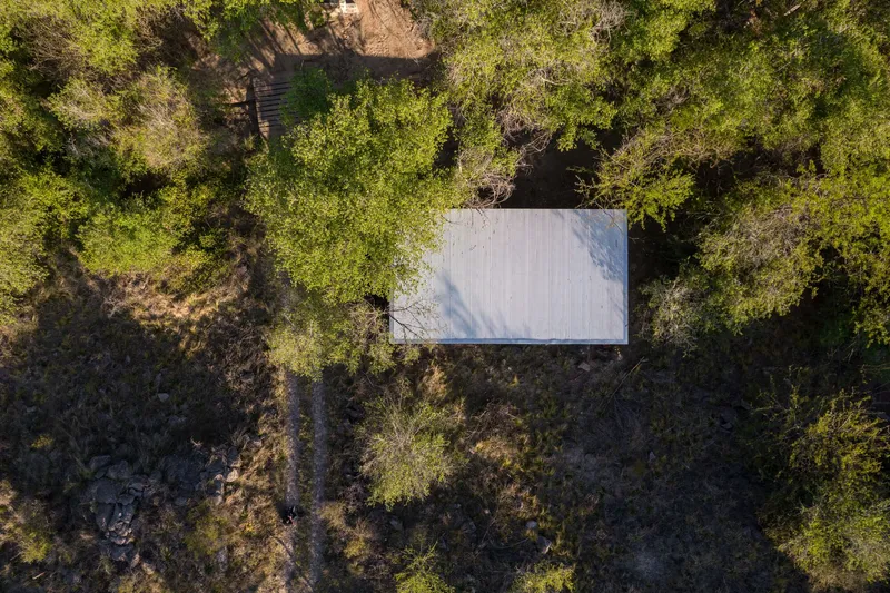 Aerial view of the rectangular corrugated metal roof surrounded by trees and cleared earth