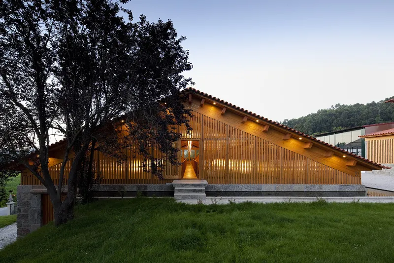 Timber-slatted facade with stone base and grass lawn framed by mature trees at dusk