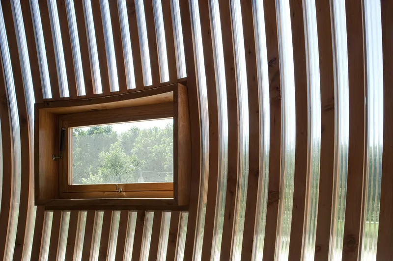 Small operable window set within vertical timber slat wall framing distant tree canopy