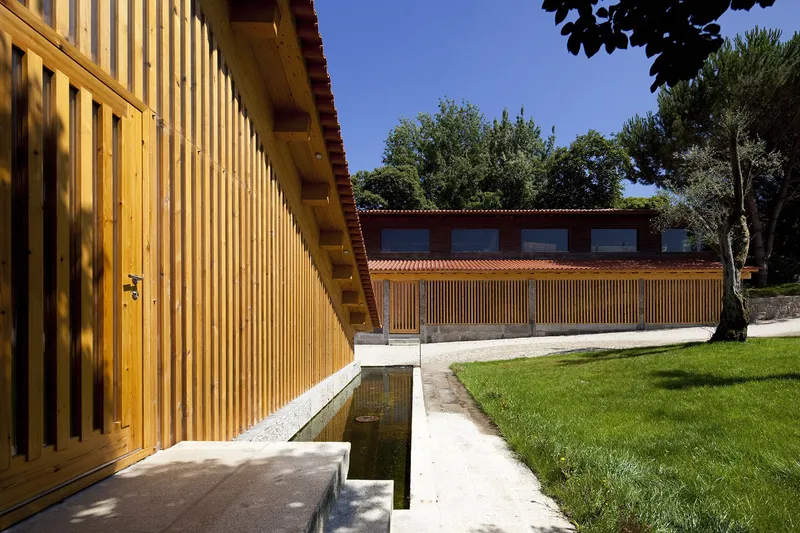 Courtyard with narrow water channel running along timber-clad walls and lawn beneath dappled tree shadows