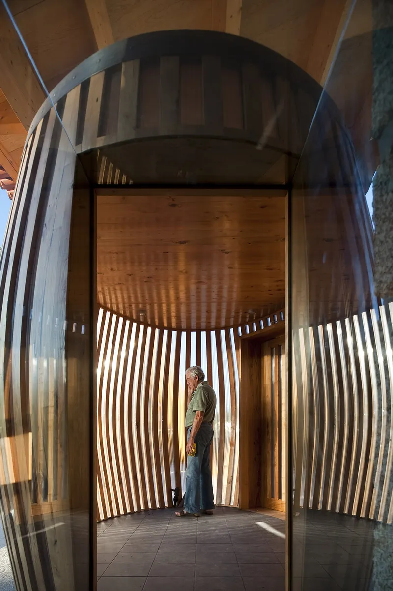 Curved timber slatted enclosure with person standing inside beneath arched opening and wooden ceiling