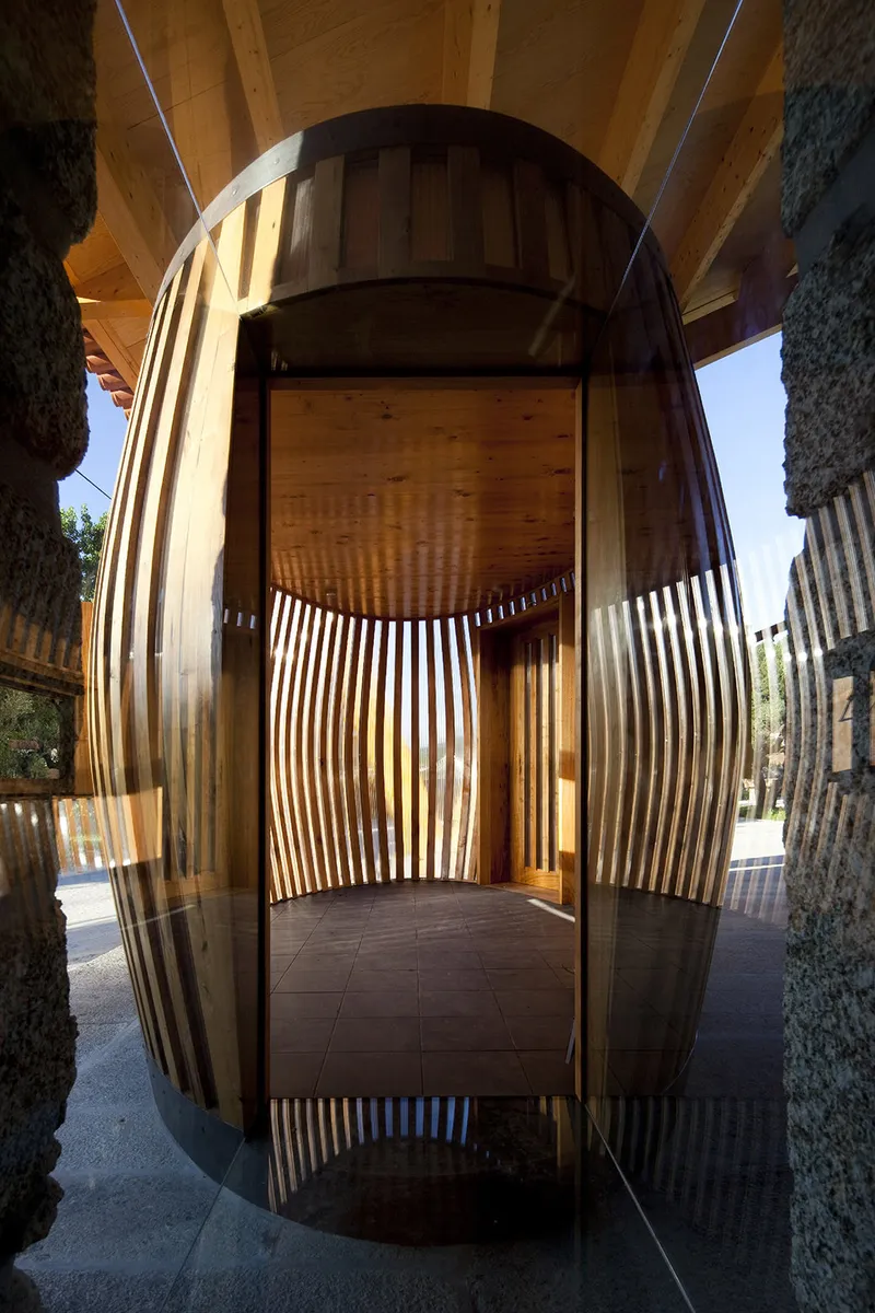 Front view of the curved slatted timber structure with stone columns flanking the entrance