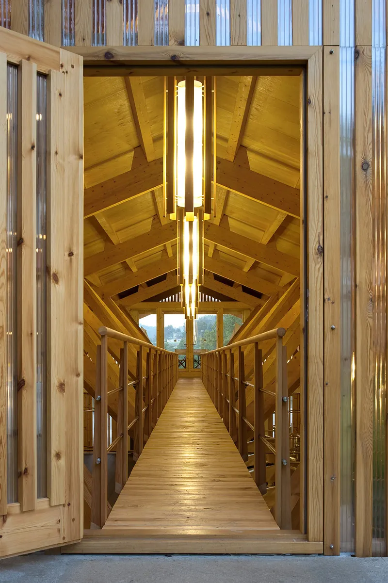Timber footbridge with exposed truss ceiling and vertical light slot framing the landscape beyond