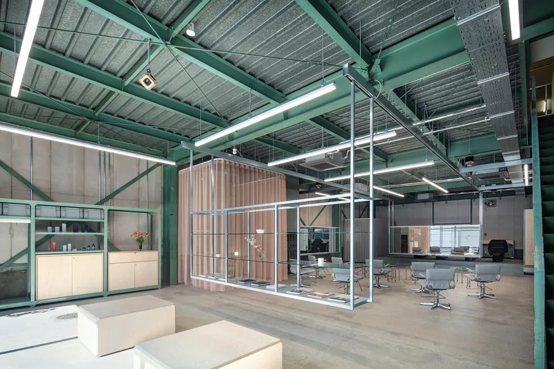 Industrial workspace with green steel structure, glass partitions and meeting room visible through white framework