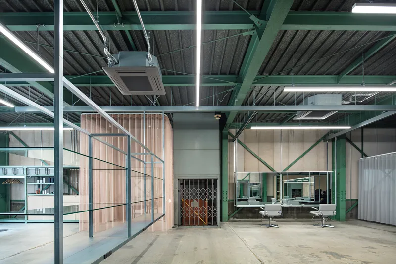 View across concrete floor toward corrugated wood partition, scissor gate and glass-enclosed meeting space