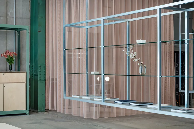 Glass shelving unit with flowers and books against a ribbed timber screen beside a green column