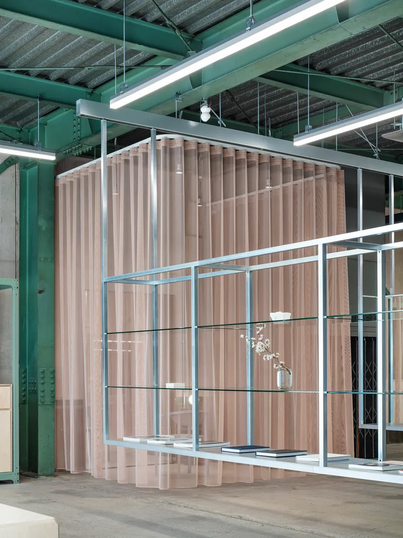 Freestanding ribbed timber partition with steel-framed glass shelving displaying flowers and objects beneath exposed ceiling beams