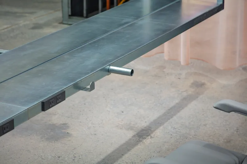 Integrated power outlet and cylindrical footrest mounted under steel desk edge on concrete floor