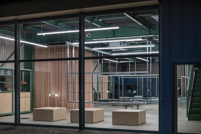 Entrance view through glazed storefront into illuminated interior with green structural frame at dusk