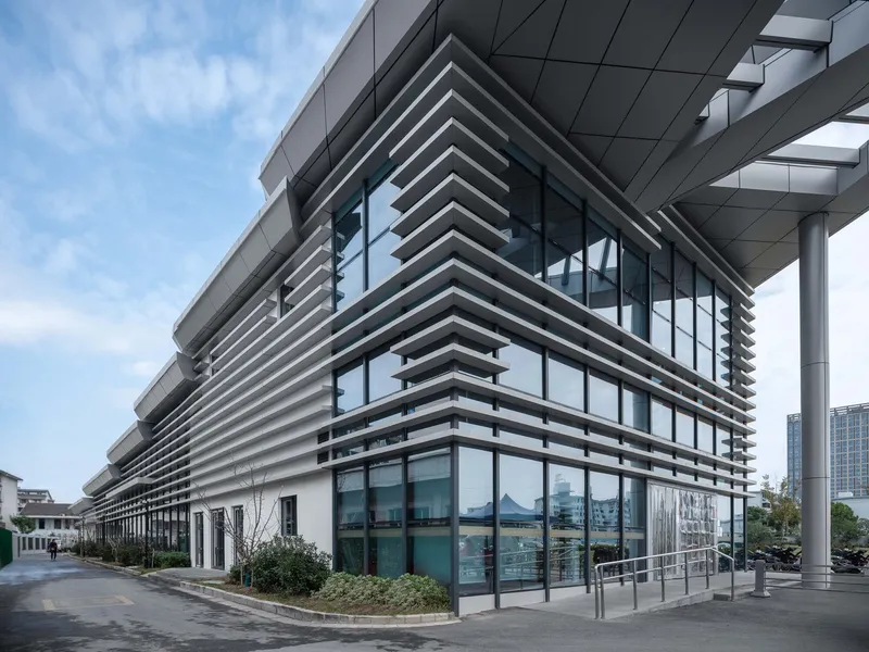 Corner view of the horizontal louvered facade wrapping the glazed ground floor with planted beds