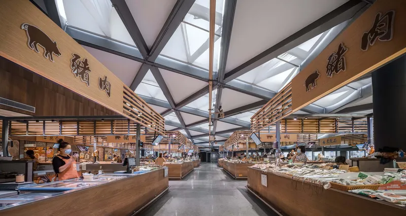 Interior market hall with timber-clad vendor stalls under an exposed steel truss and glazed roof structure