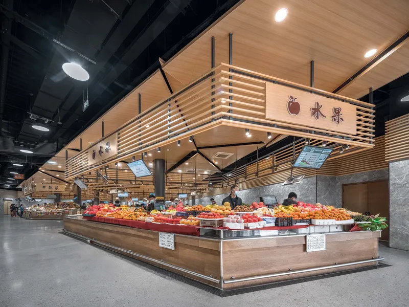 Fruit vendor stall with horizontal wood slat screens and suspended timber ceiling panels under artificial lighting