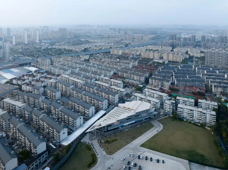 Aerial view of the building with layered rooflines surrounded by rows of residential blocks in hazy light
