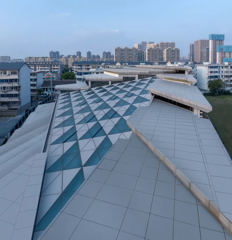 Rooftop view of the folded metal panel system with diagonal teal-tinted glazing at dusk
