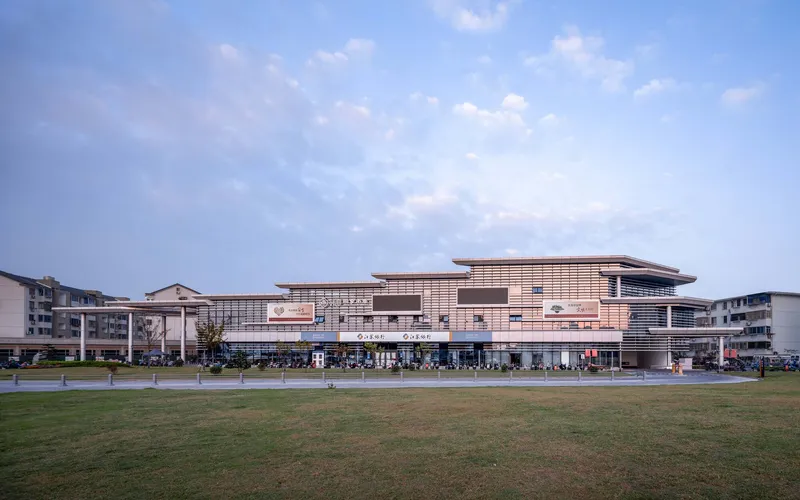 Facade with horizontal louvered upper volumes above glazed storefronts facing a green lawn in late afternoon light