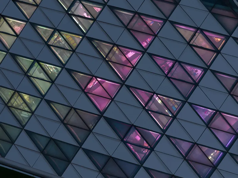 Close-up of the triangular glazed panels with pink and amber interior lighting at twilight