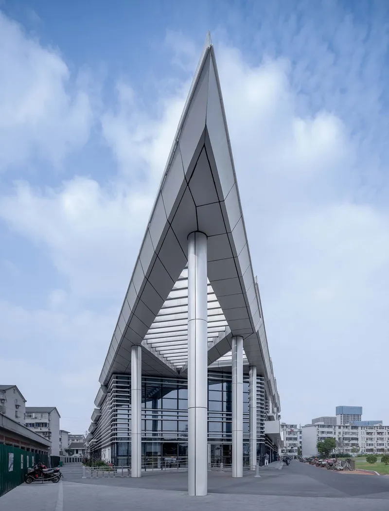 Upward view of the triangular canopy point supported by white columns against a partly cloudy sky
