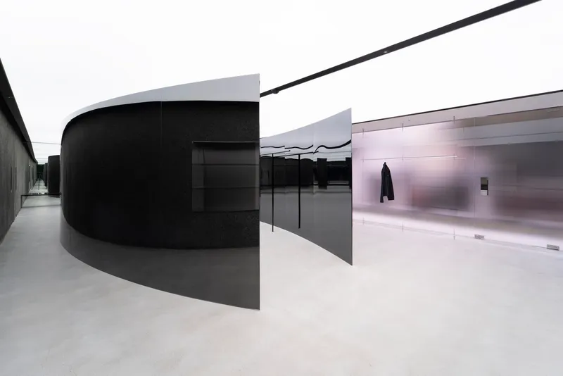 Curved black metal volume alongside polished metal panels with pale resin flooring under diffused daylight