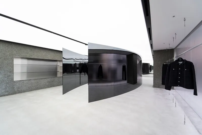 Retail interior with black curved partition walls and textured stone surfaces under a continuous skylight
