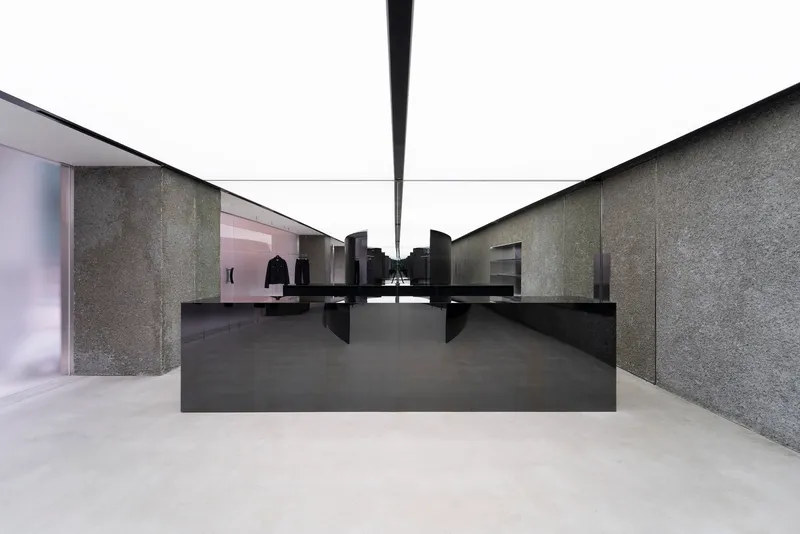 Black steel counter centered between textured stone walls and translucent glass partitions in a daylit gallery