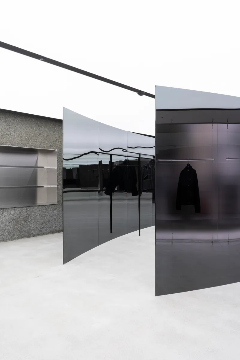 Retail interior with black glass partitions, terrazzo walls, and clothing racks under white painted ceiling