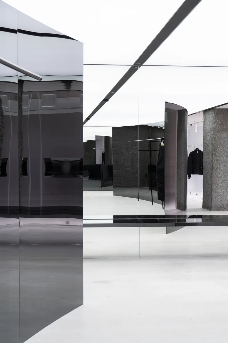 Open sales floor showing layered glass panels, curved dark metal displays, and polished terrazzo columns